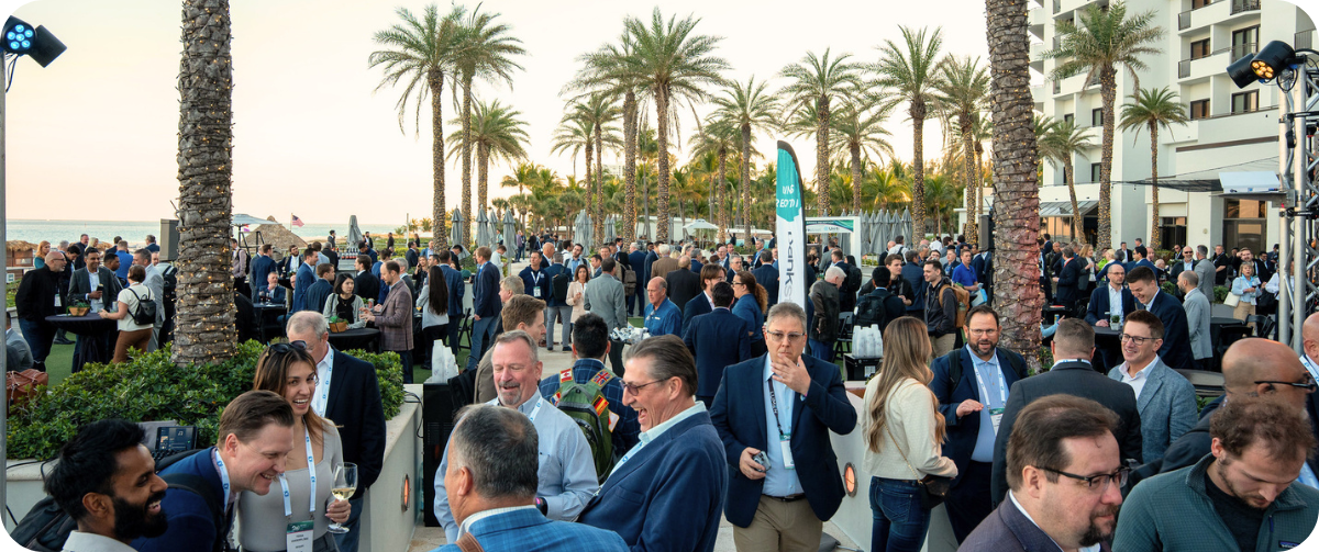 A busy outdoor networking reception at Metro Connect USA, with attendees connecting among palm trees beside the beachfront resort, overlooking the ocean.