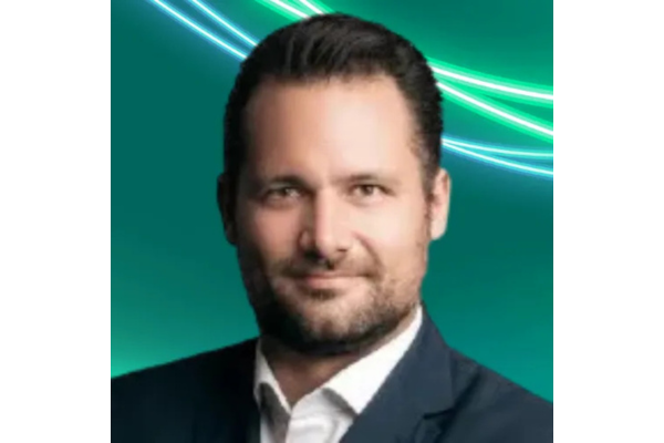 Professional headshot Jan Vesely with short, styled dark hair and a neatly trimmed beard. He is wearing a dark suit jacket over a white open-collared shirt. The background is teal with glowing green and white abstract lines curving across the top right.