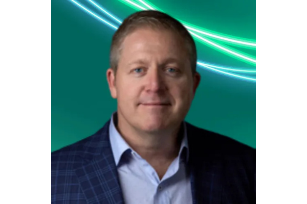 Professional headshot of Joe Scattereggia with short brown hair, wearing a dark plaid blazer over a light blue collared shirt. The background is teal with glowing green and white abstract lines curving across the top.