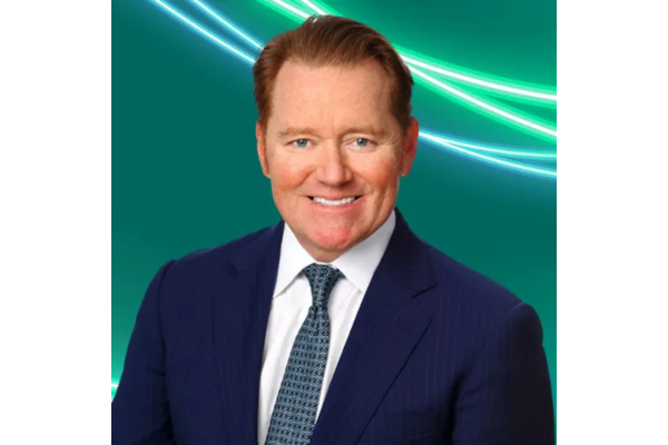 Professional headshot of a Marc Ganzi with slicked-back reddish-brown hair, wearing a dark blue suit jacket, a white shirt, and a blue patterned tie. The background is teal with glowing green and white abstract lines curving across the top.