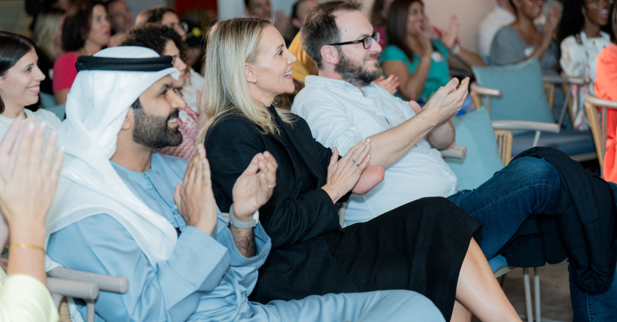A group of people sitting in a gathering, clapping and expressing appreciation.