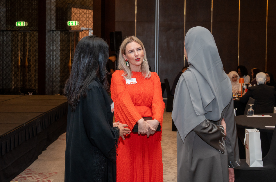 Three women engaged in conversation at a formal event, with one wearing a gray hijab and another in a black outfit.