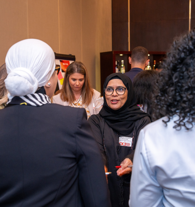 A group of people, including a woman wearing a hijab, engaged in conversation at a social event.