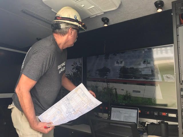 man in a van, looking at a screen, holding a blueprint