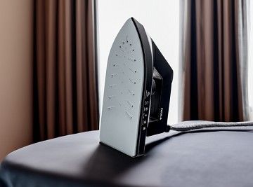 Hotel room iron placed upright on an ironing board with window light in the background