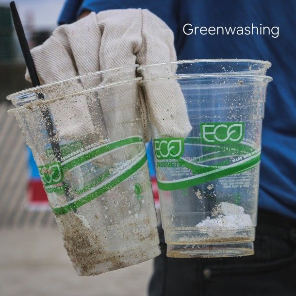 Close-up of gloved hand holding eco-branded plastic cups with visible beach sand, representing greenwashing and misleading environmental claims in product marketing.