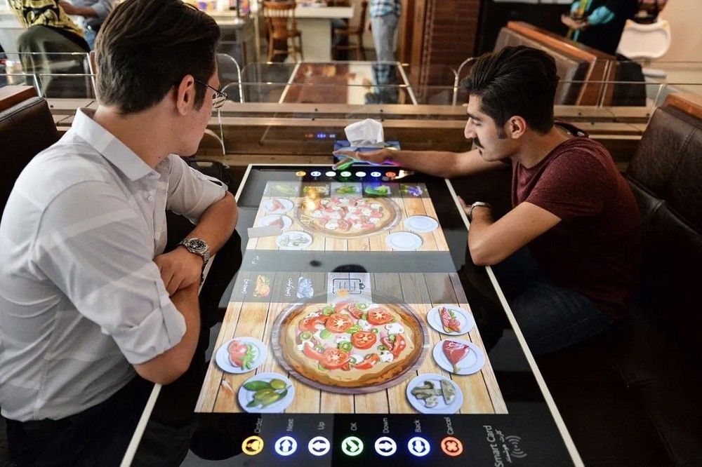 Two diners using a touchscreen table to order pizza in a tech-enabled restaurant