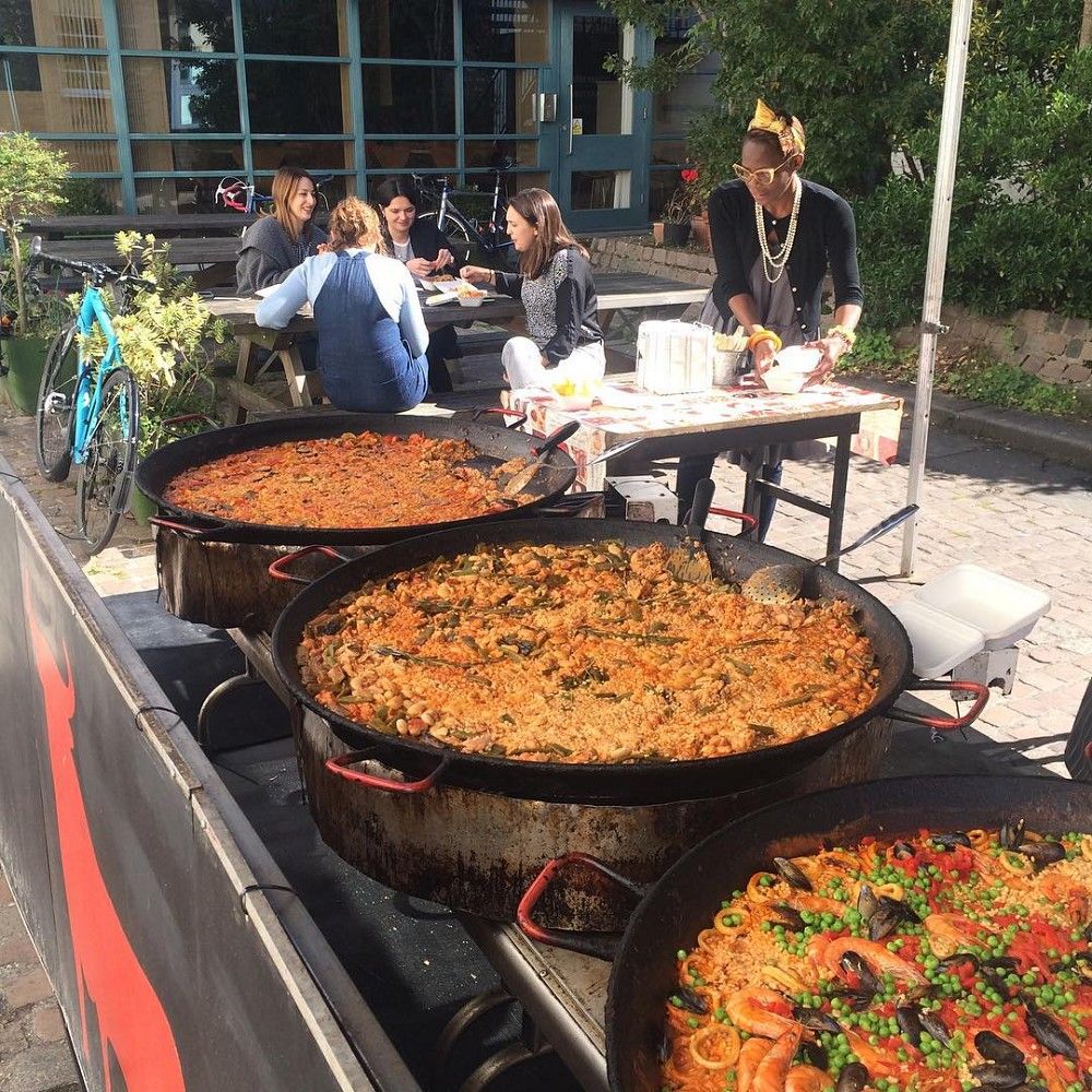 Large paella pans cooking outdoors at a UK street market with customers dining.