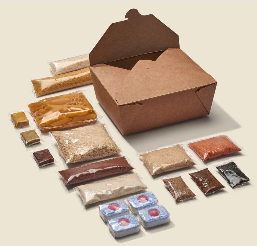 Brown cardboard meal kit box surrounded by individually portioned ingredients in plastic-free, biodegradable wrappers—showcasing Xampla’s sustainable packaging innovation with Gousto