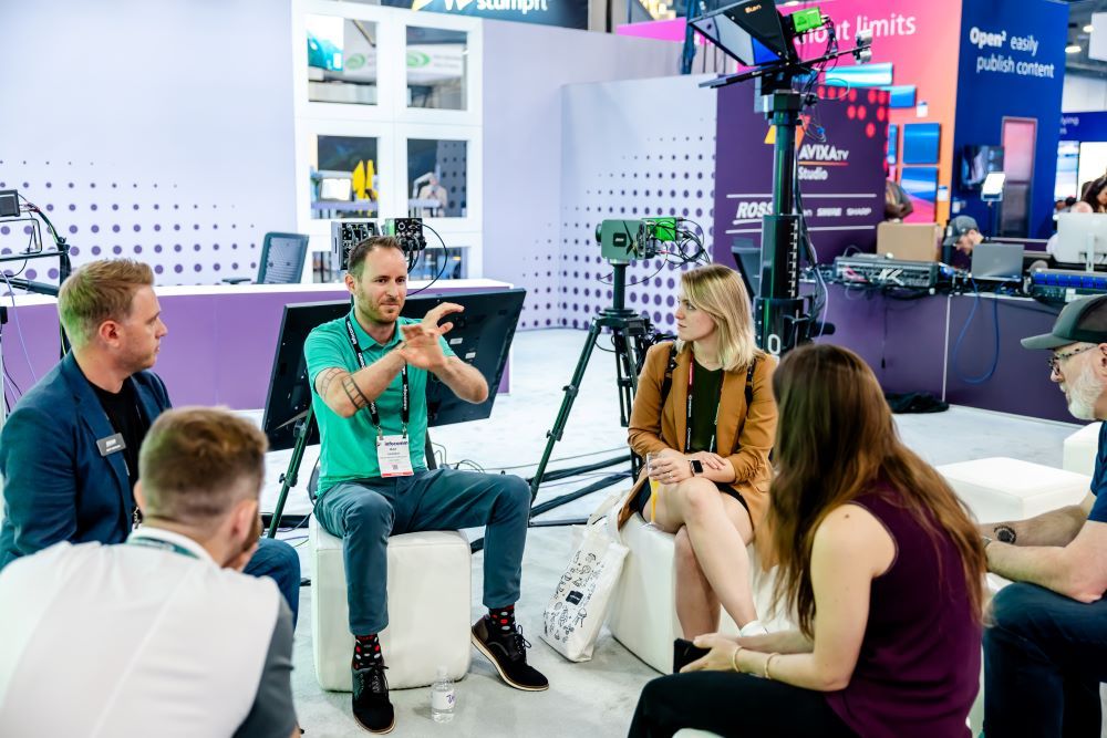 A group of InfoComm attendees talk with one another in the AVIXA TV booth.