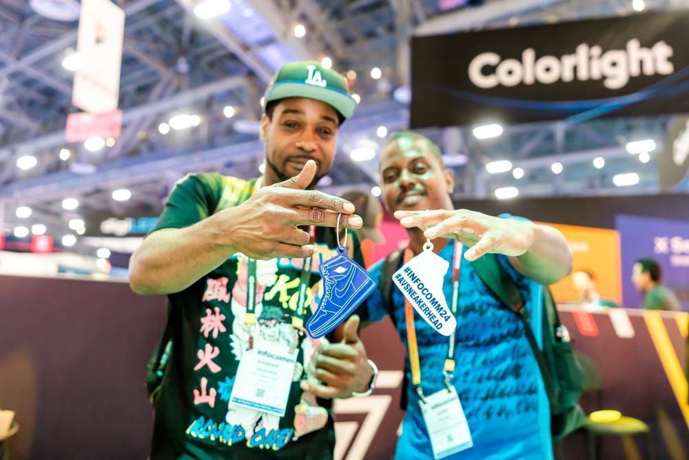 Two InfoComm attendees hold up small shoe cards that say #AVSNEAKERHEAD