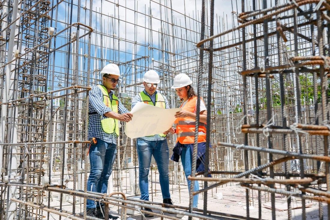 A picture of two men and one woman on a construction site in hard hats looking at a piece of paper. 