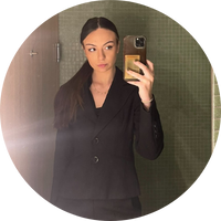 Woman with black hair standing in grey-tiled bathroom, holding an iphone