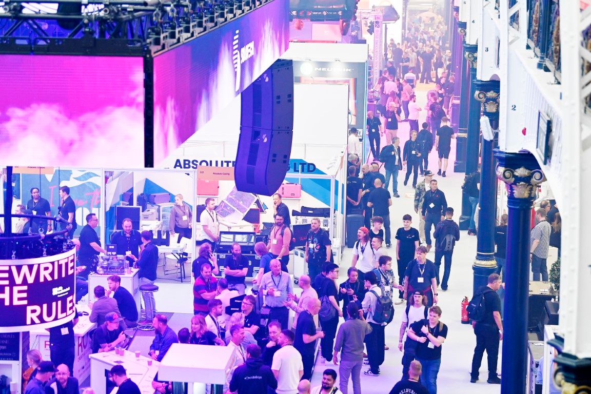 a crowd of people gathered and chatting around a trade show stand