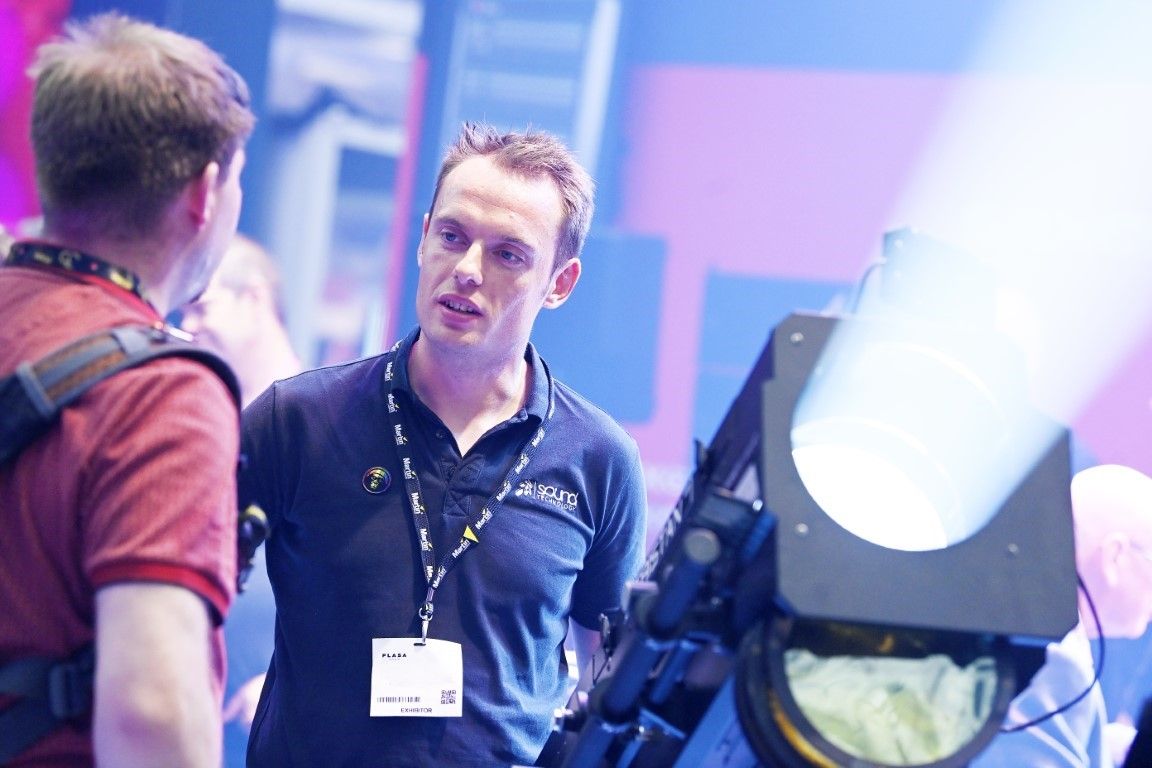 Sound technology exhibitor talking to visitor with light beaming to the right at plasa show 2024