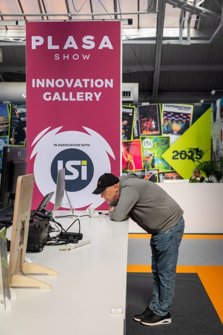 A man in a white T-shirt looks closely at a large moving-head stage light on display on the Innovation Gallery at PLASA Show London 2025.