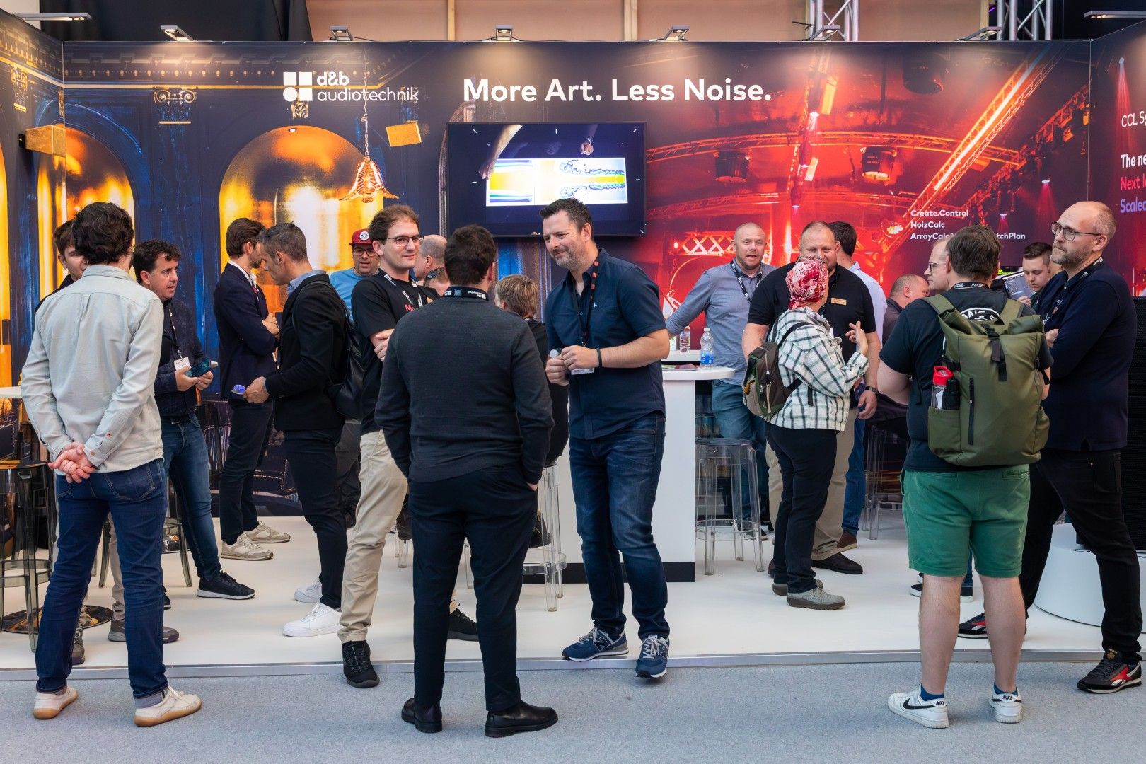 Visitors gather and network at the d&b audiotechnik stand at PLASA Show London 2025, in front of a backdrop reading ‘More Art. Less Noise.