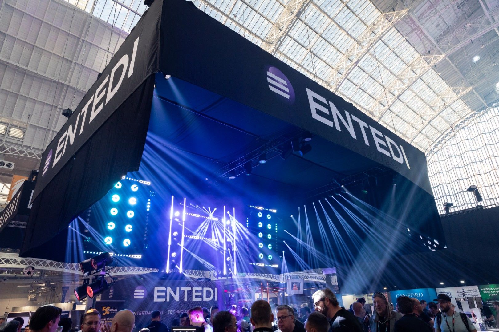ENTEDI stand at PLASA Show London 2025 inside Olympia London, featuring bright stage lighting beams and LED displays drawing a large crowd of visitors