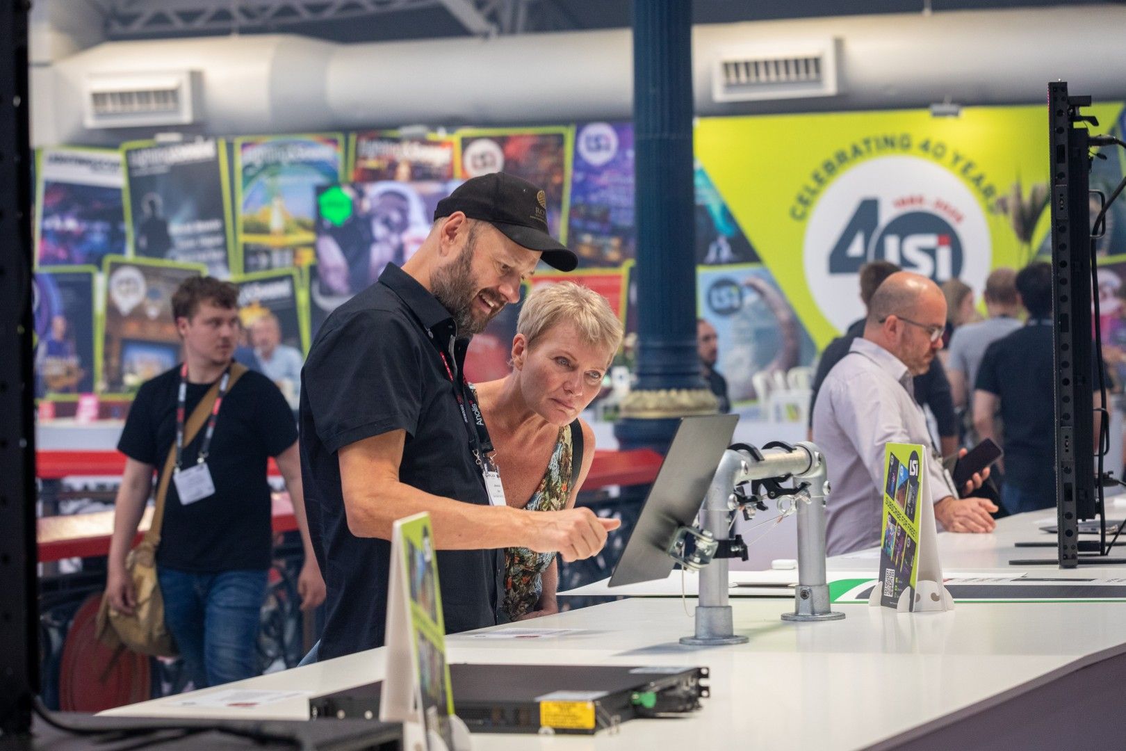 A male exhibitor with a beard and black cap dissusses a product with a female visitor with short blonde hair at the LSi Innovation Gallery during PLASA Show London 2025.