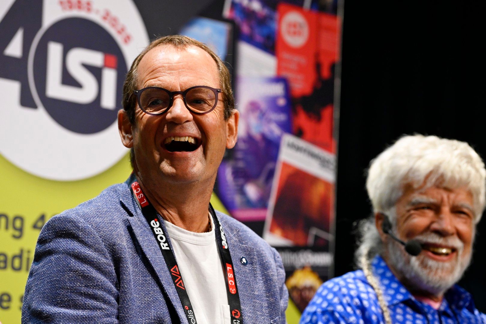 Two male speakers - Dave Crump and Tony Andrews, Founder of Funktion-One, smiling on stage during a seminar at PLASA Show London 2025, with LSi Magazine 40th anniversary branding in the background