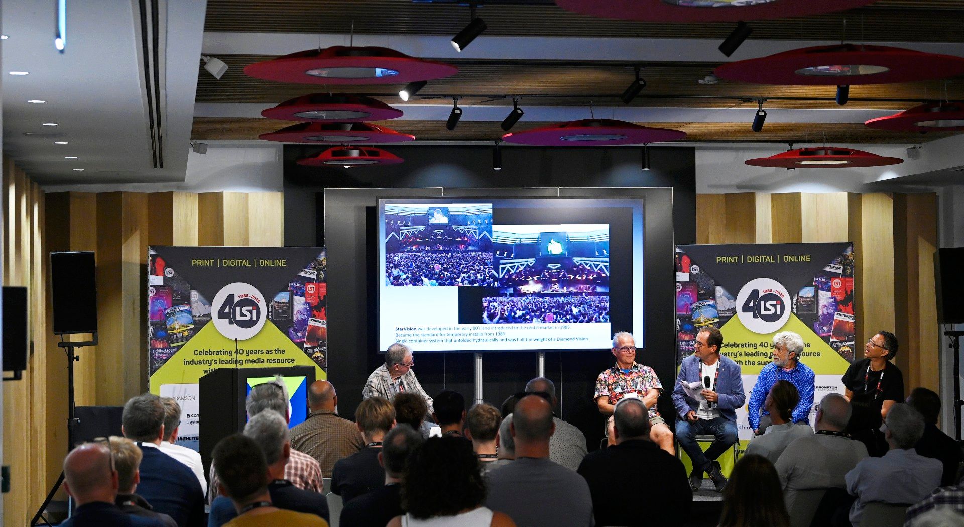 Audience attending an LSi Theatre panel discussion at PLASA Show London 2025, featuring five speakers seated on stage in front of a screen showing event visuals, with banners marking LSi Magazine’s 40th anniversary.