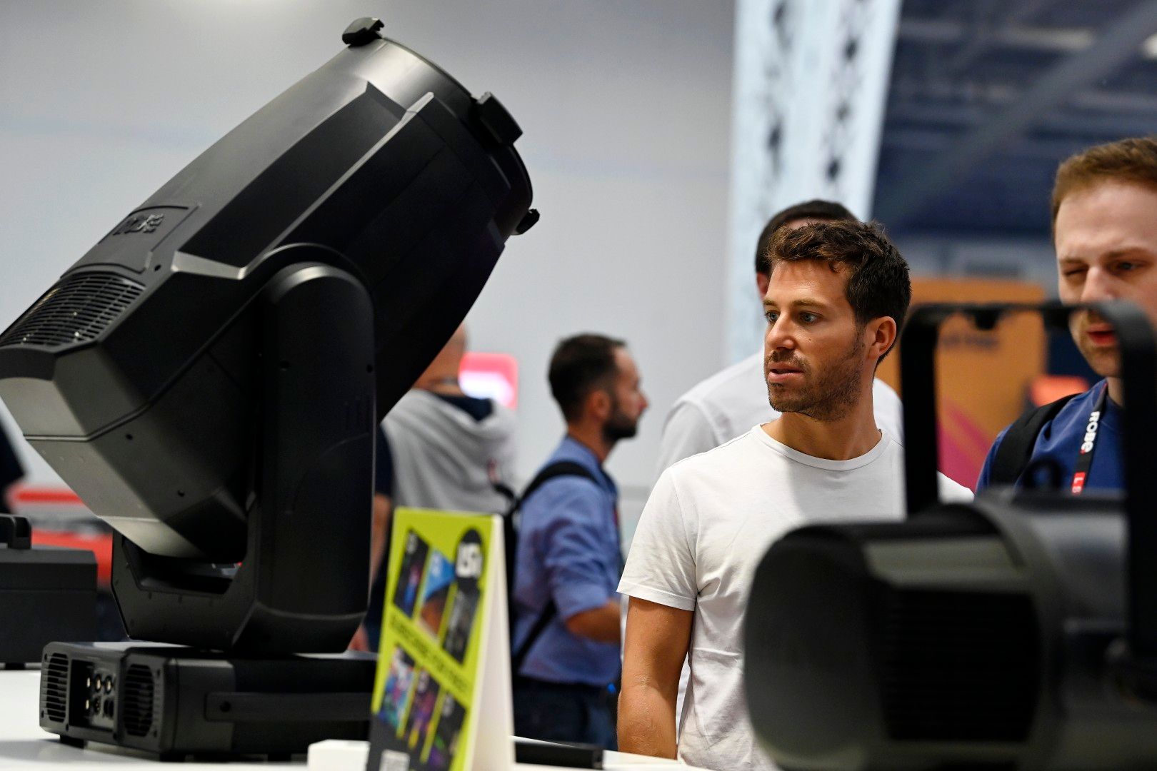 A man in a white T-shirt examines a large moving-head stage light on display on the Innovation Gallery at PLASA Show London 2025.