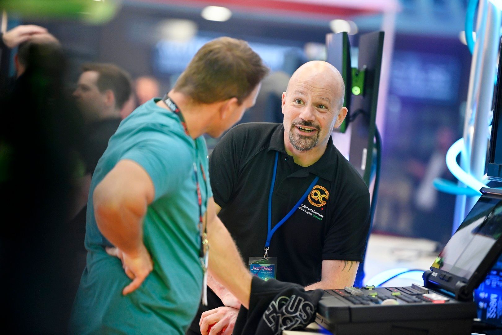 Exhibitor from A.C. Entertainment Technologies speaks with a visitor at PLASA Show London 2025, demonstrating lighting control equipment on the stand.