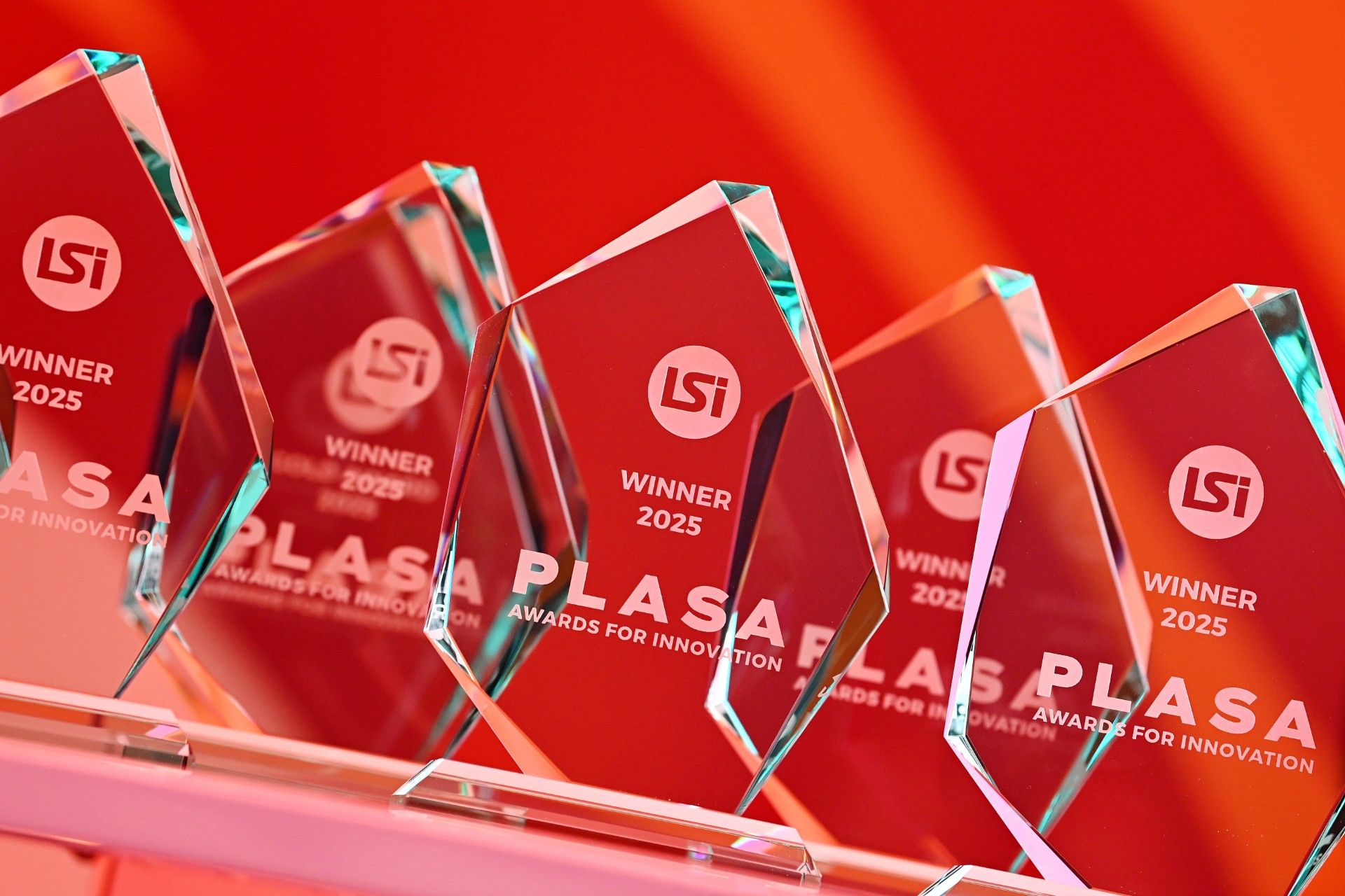 Close-up of the 2025 PLASA Awards for Innovation trophies, presented in association with LSi magazine, featuring crystal-cut glass awards on a red background.