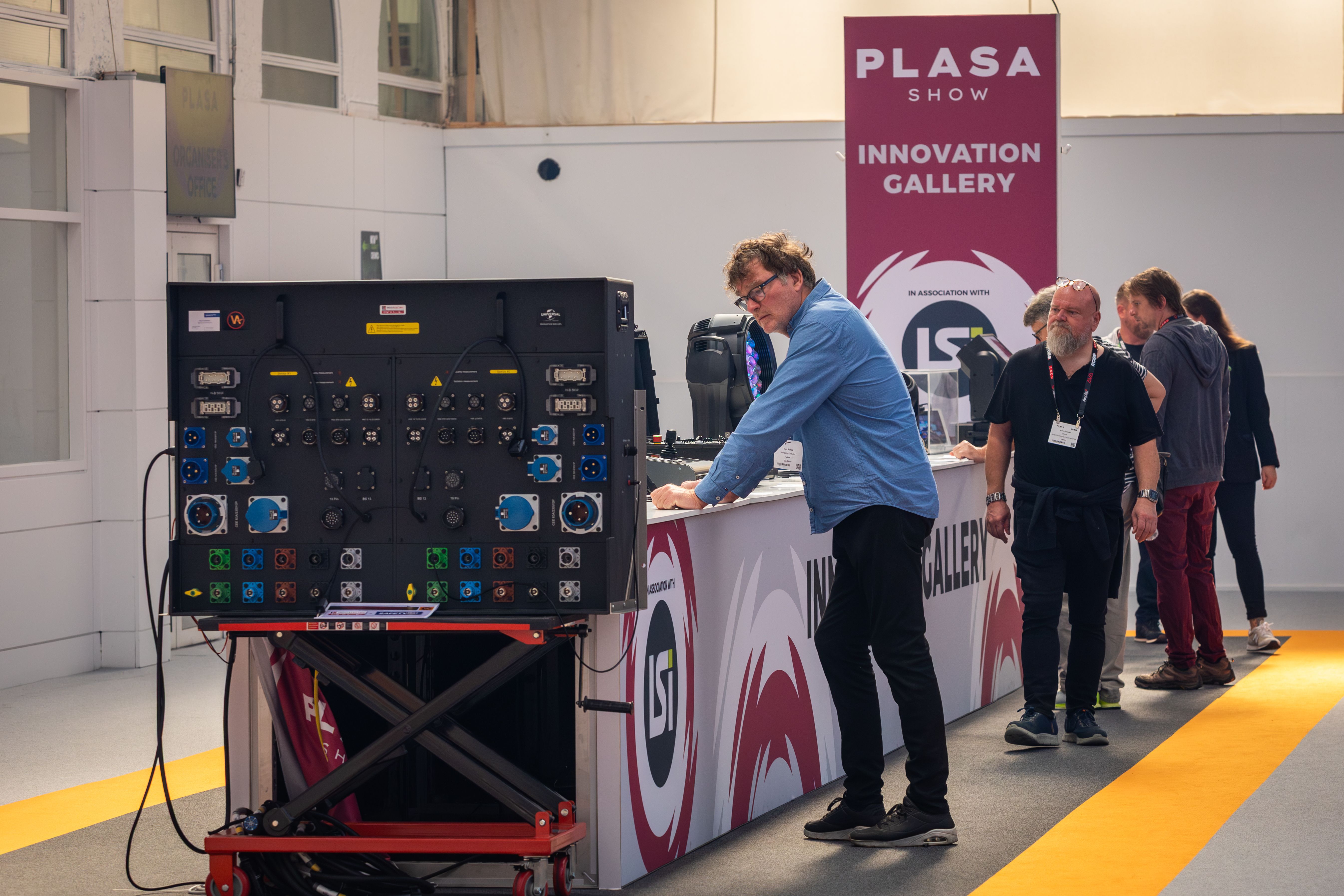 A group of attendees gathered around the Innovation Gallery counter looking at technology showcases under a pink PLASA Show banner.