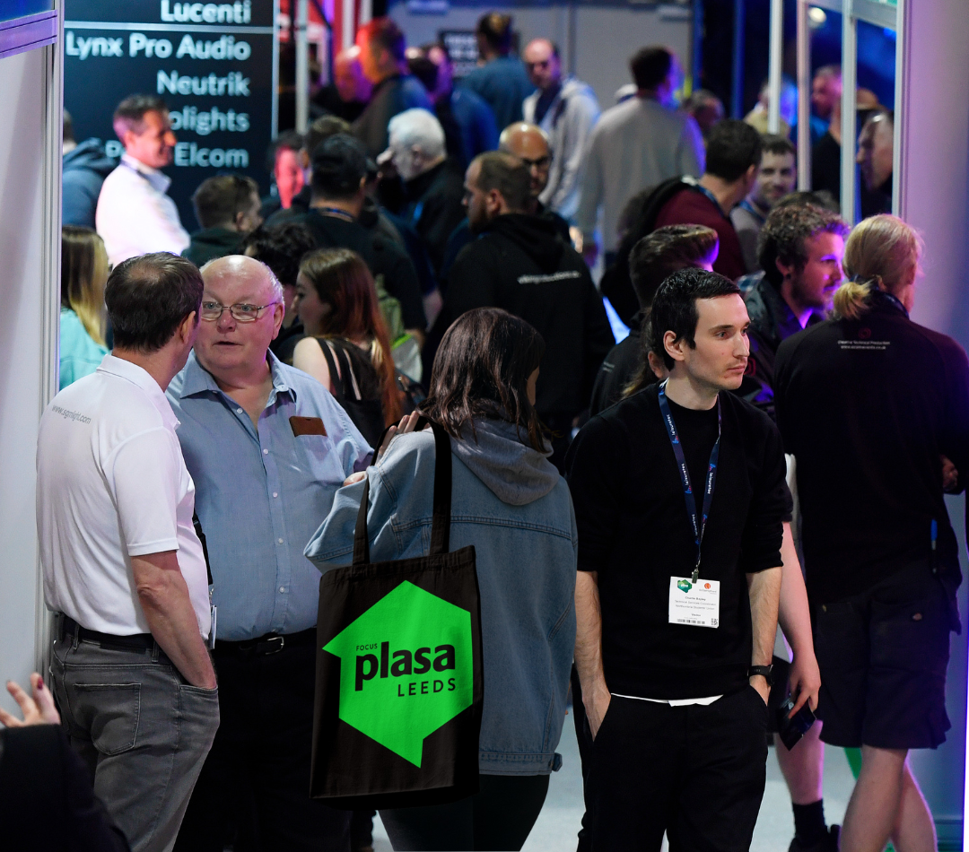crowded show floor focusing on woman walking and holding a PLASA Leeds fabric tote bag