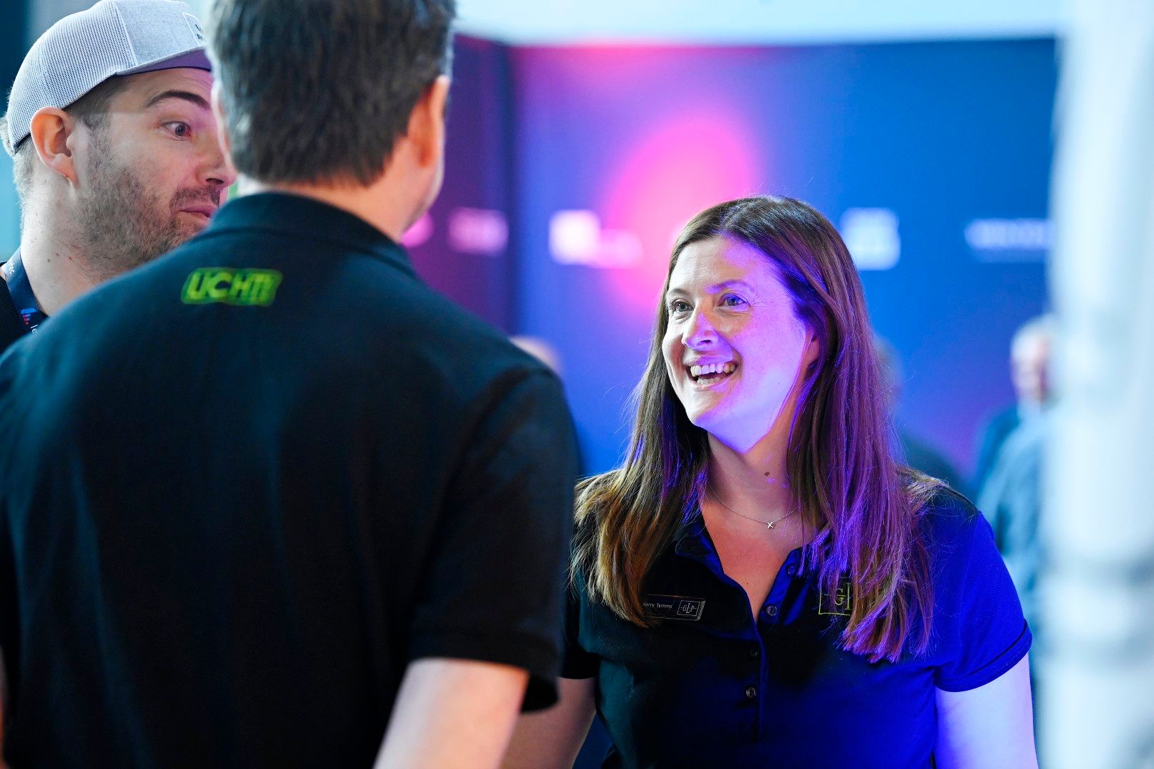 Female exhibitor laughing with two male visitors at PLASA Focus Leeds 2024