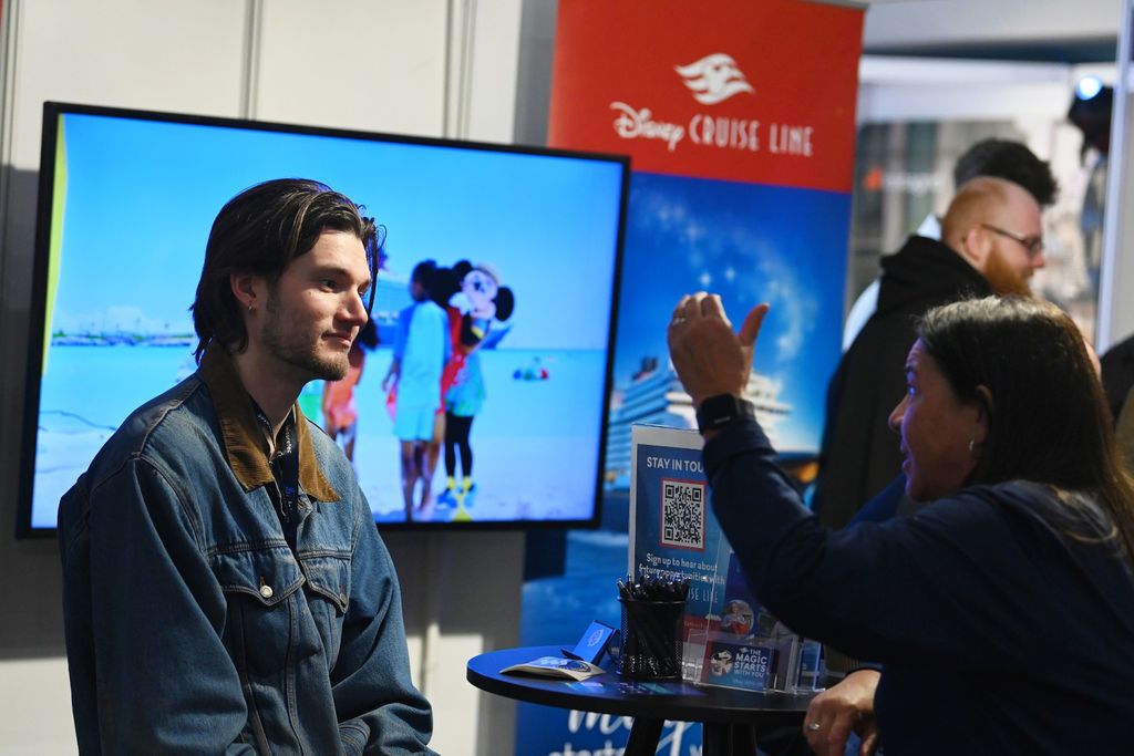 oung man speaks with a woman at the Disney Cruise Line stand during PLASA Focus Leeds, with a large promotional screen and recruitment display in the background.