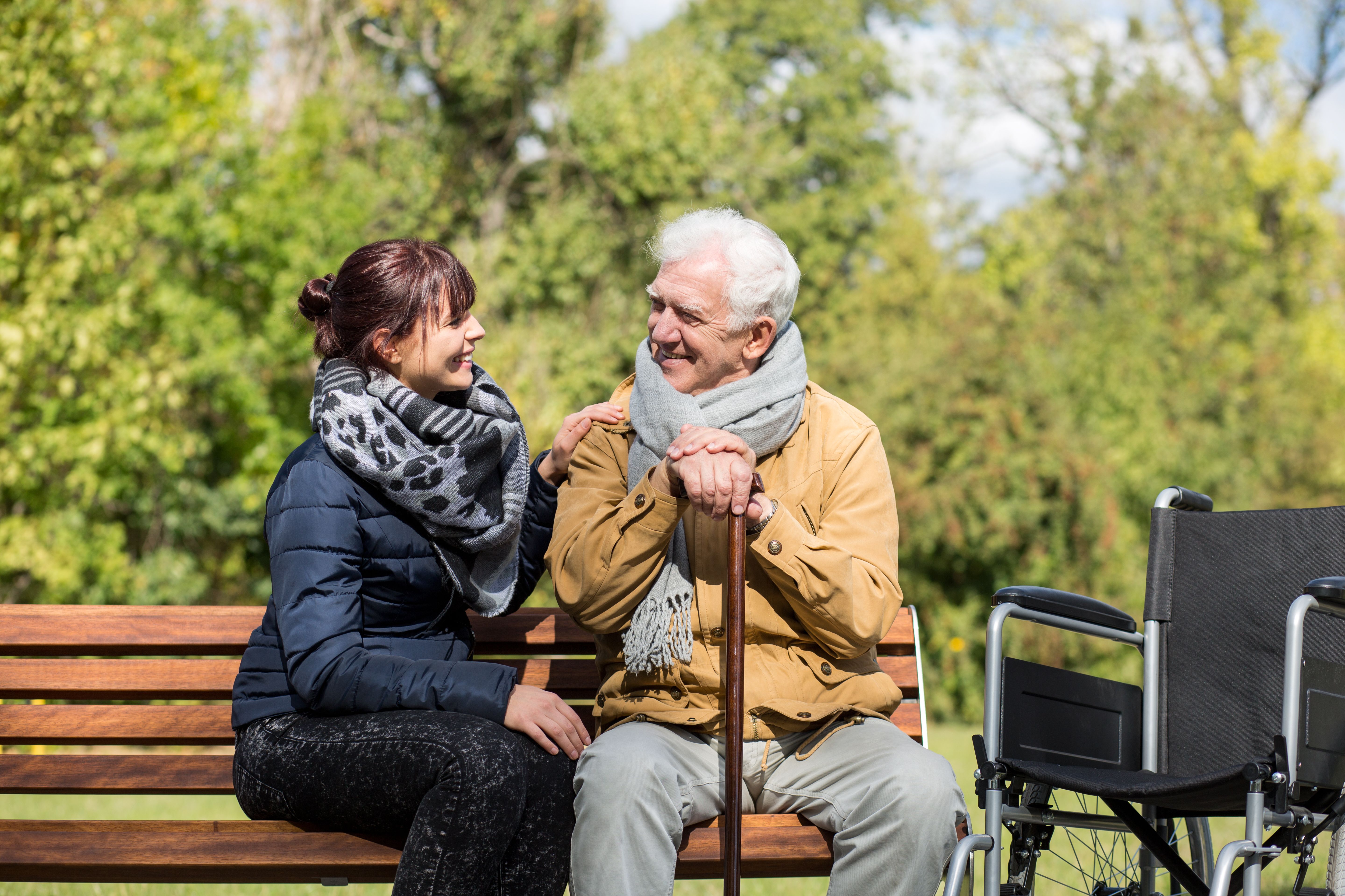 Picture of a man and a woman sat next to each other in a park on a bench looking towards each other smiling