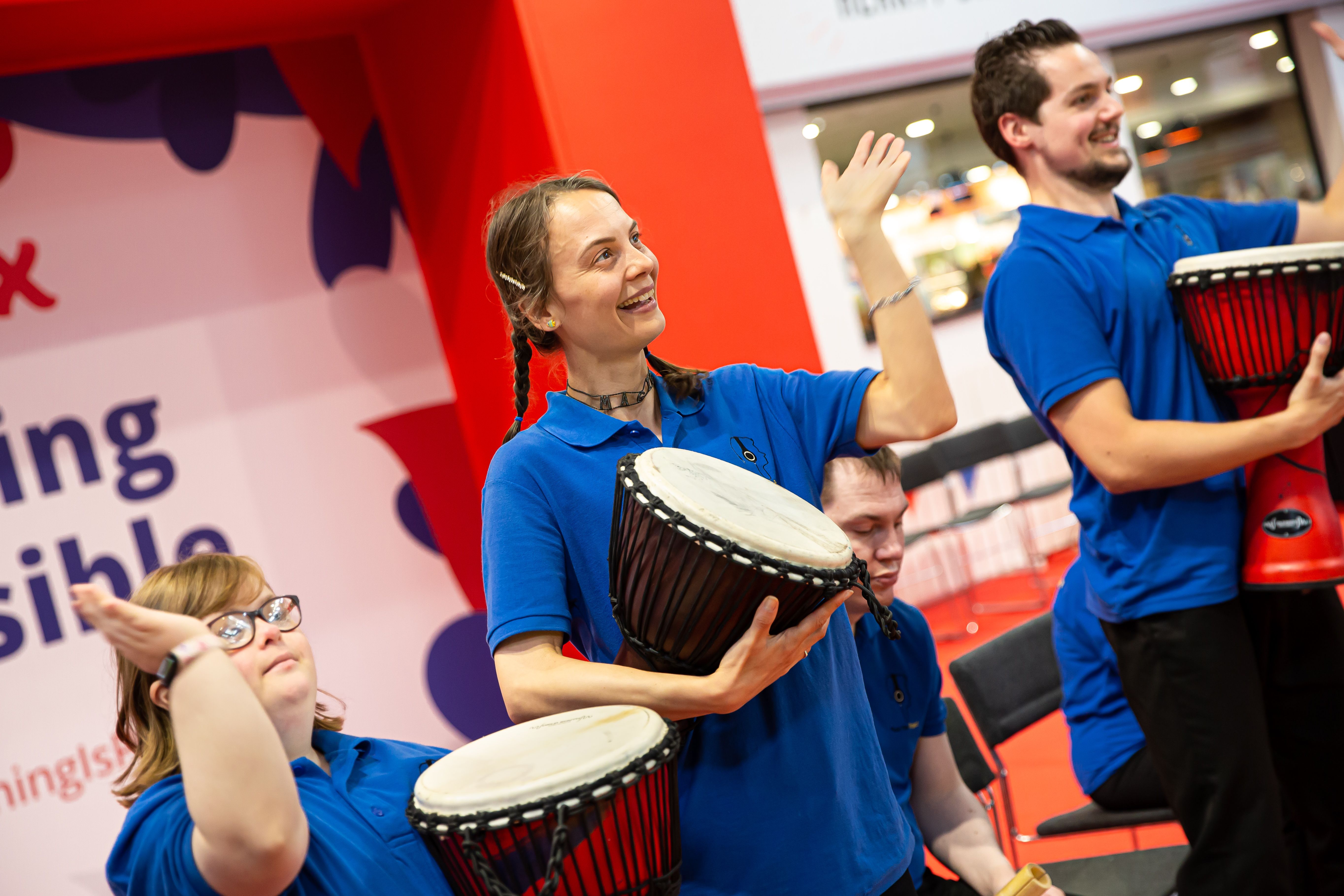 Three people are performing with drums, they are smiling. 