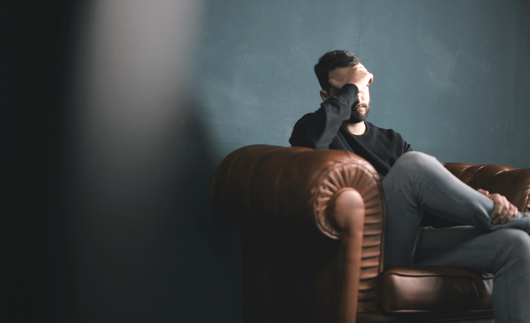 Person sitting on a sofa resting their head on their hand.