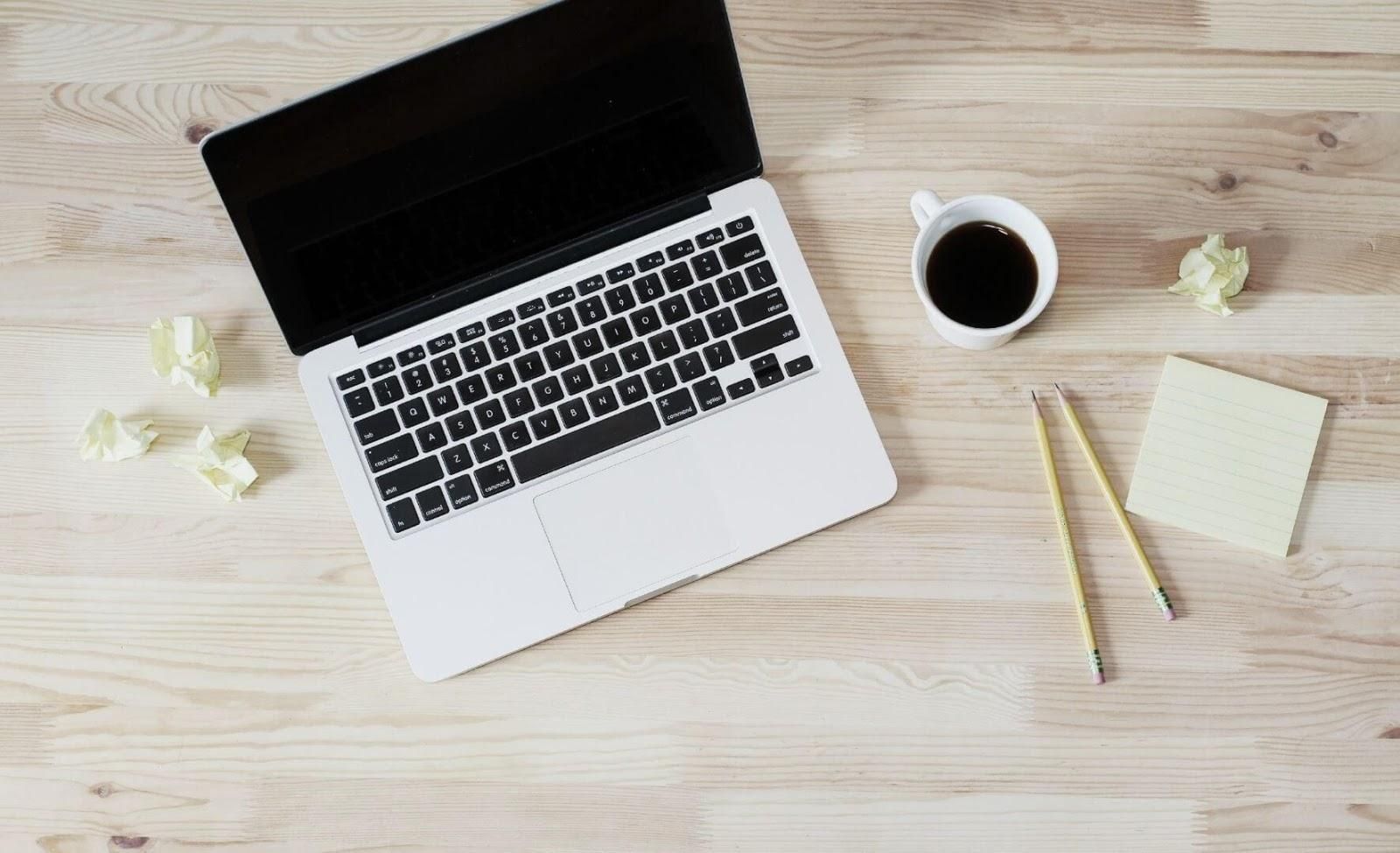 Picture of a laptop, sticky notes, pencils and coffee mug on a table.