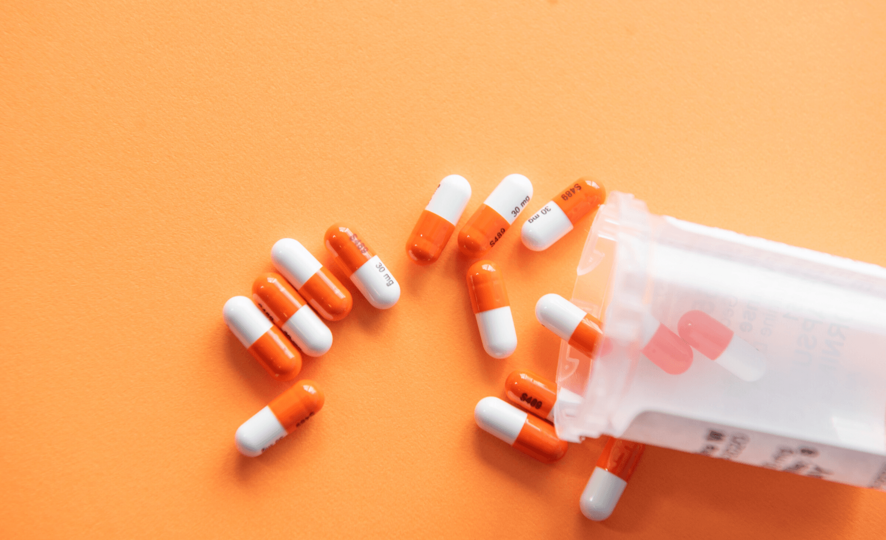 Picture of a tub of pills spilled on an orange background