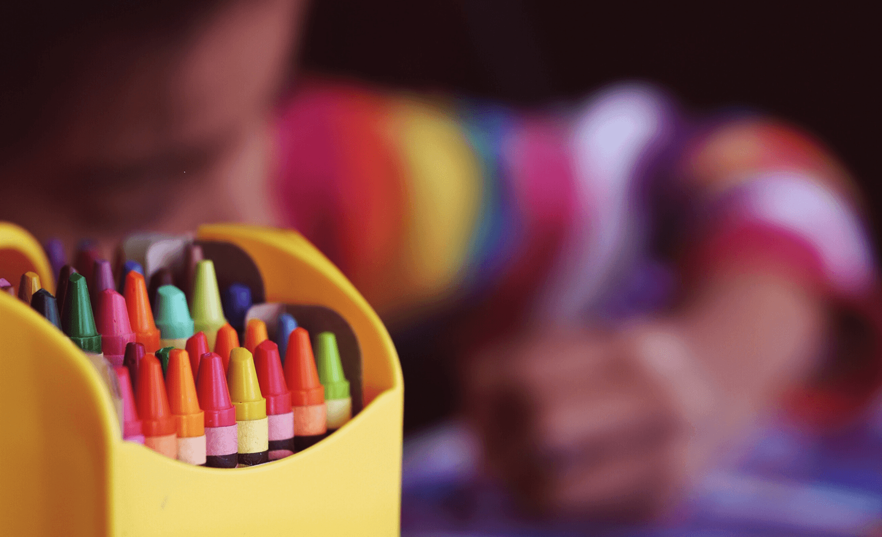 Picture of a box of crayons with a kid blurred in the background.