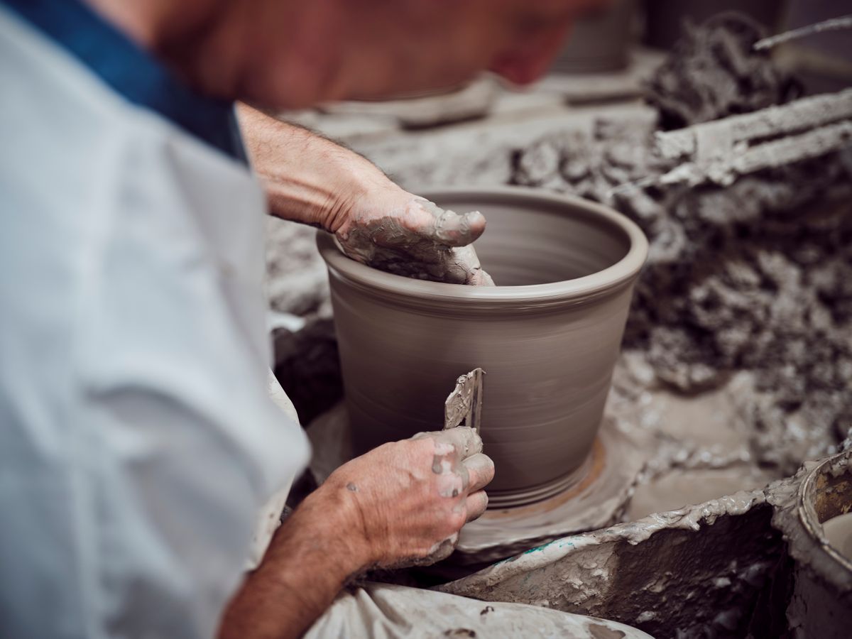 A potter's hands shape a clay pot on a spinning wheel, conveying craftsmanship and focus. The environment is earthy and textured with clay.