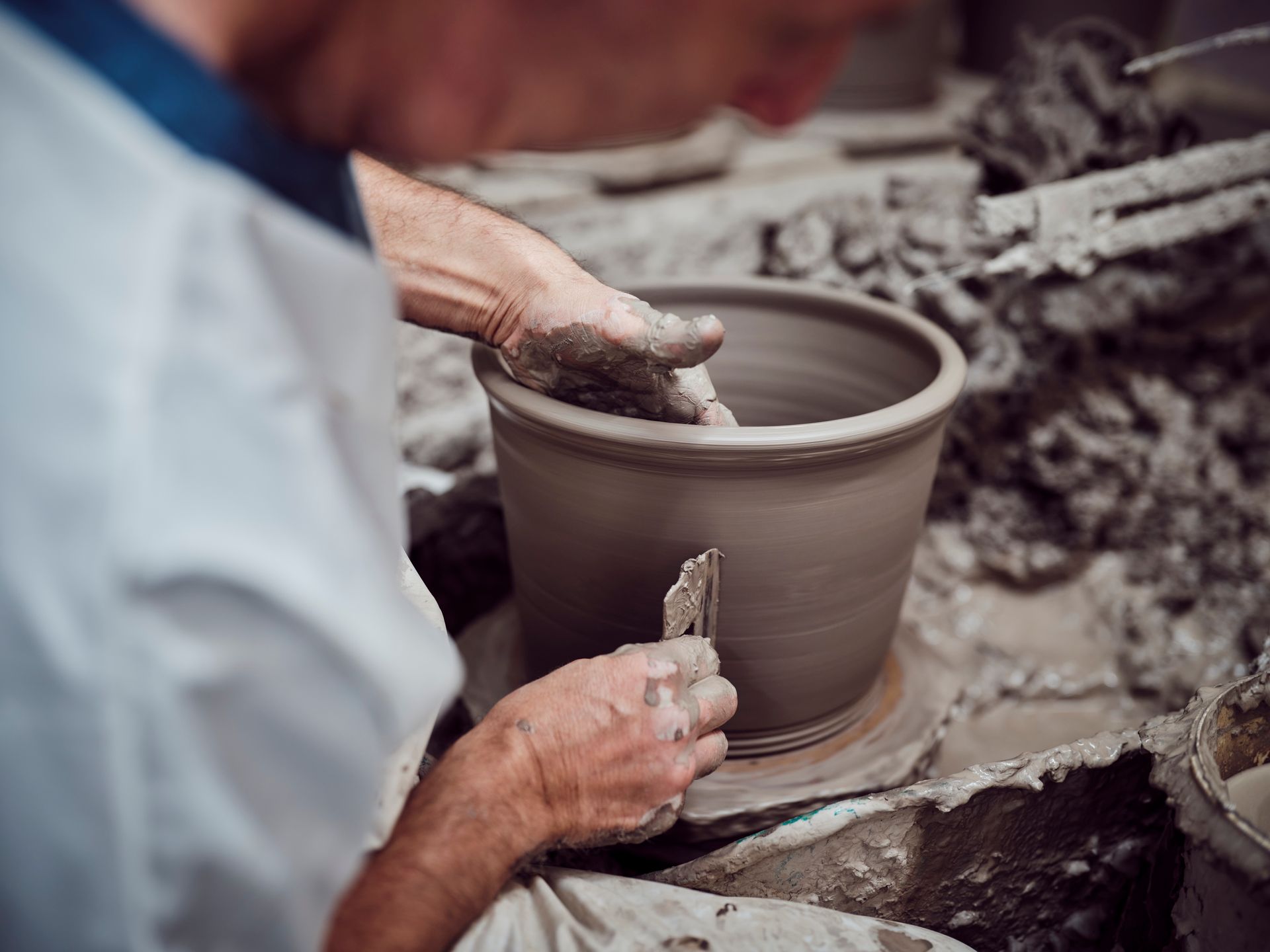 A potter's hands shape a clay pot on a spinning wheel, conveying craftsmanship and focus. The environment is earthy and textured with clay.