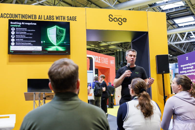 A speaker presenting at a booth for AccountingWEB AI Labs with Sage, with an audience seated in front and a screen displaying information about controlling AI.