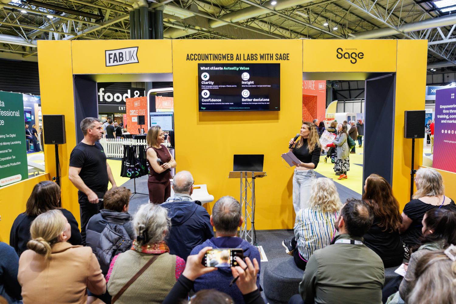 A presentation at an event with a large screen displaying information about accounting, while an audience listens attentively.