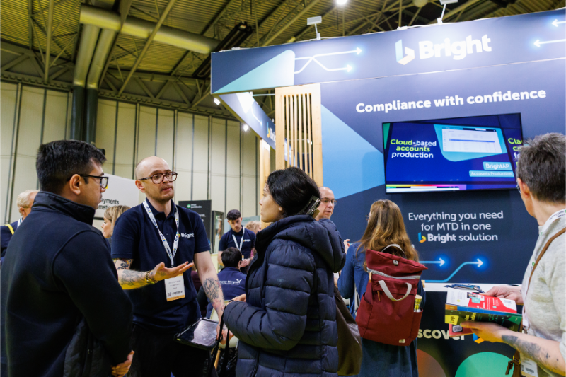 A booth at an event featuring the Bright brand, with a group of people engaged in conversation and looking at a presentation screen.