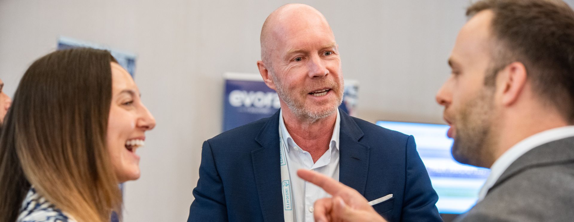 Engineer wearing a yellow hard hat operating a futuristic touchscreen interface in a factory, with robotic arms working on an assembly line. 