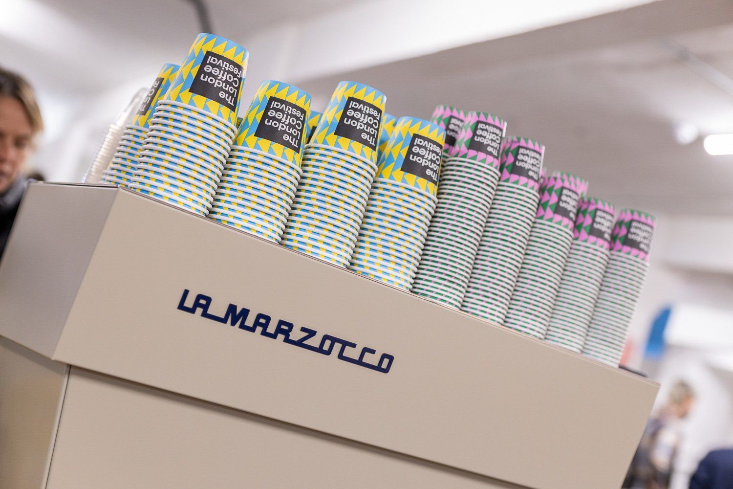 London Coffee Festival branded takeaway cups stacked on a La Marzocco espresso machine